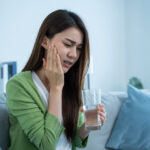 舌のヒリヒリにリリカ(プレガバリン)は効く?歯科医師が分かりやすく解説 Asian beautiful woman feel terrible toothache after drink cold water. Attractive female sit on sofa in living room touching cheek, feel hurt and suffering from sensitive tooth ache, pain and cavities.