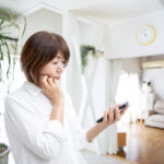 A worried woman using her smartphone, Japanese middle-aged woman, living room at home